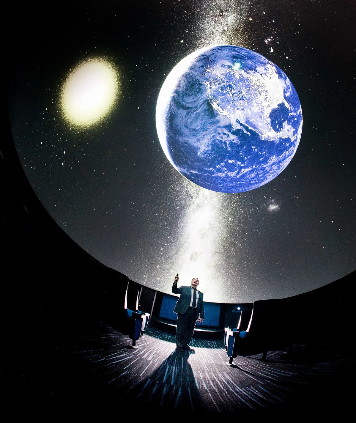 Image of a planetarium with a model of earth suspended in the air and a man standing under it pointing towards it.